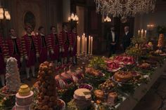 a long table filled with lots of food and people in uniform standing behind it next to candles