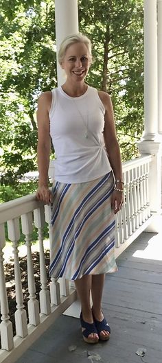 a woman standing on a porch next to a white railing with trees in the background