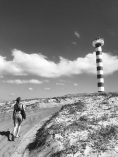 a man walking down a dirt road next to a light house on top of a hill