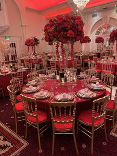 a table set up for a formal dinner with red flowers in vases and place settings