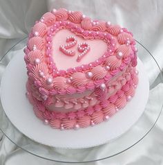 a heart shaped cake with pink icing and pearls on it's edges, sitting on a glass plate