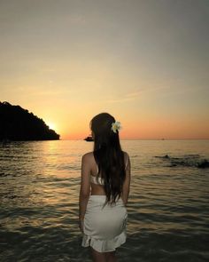 a woman standing in the water at sunset with her back to the camera, looking out into the ocean