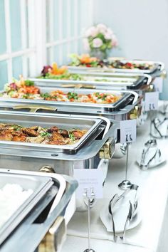 a row of buffet style trays with food on each one side and place cards in the middle