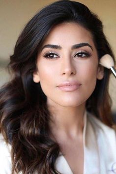 a woman with makeup brushes in her hand and looking at the camera while wearing a white suit