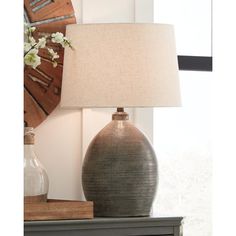 a table lamp sitting on top of a dresser next to a vase with flowers in it