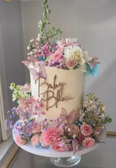 a white cake with pink and blue flowers on top is sitting in front of a window