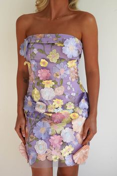 a woman wearing a purple dress with flowers on it and her hands in her pockets