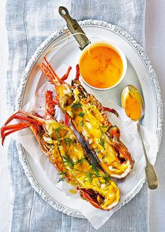 two lobsters on a plate with dipping sauce and a spoon next to it,