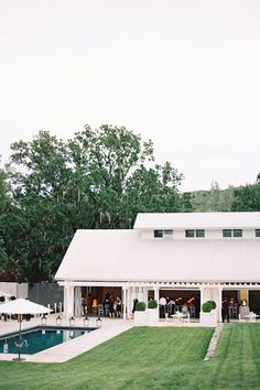 a large white house with a pool in the front yard and people sitting at tables outside