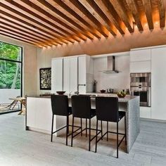 an open kitchen and dining area with white cabinets, black bar stools and wooden ceiling