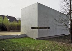 a concrete building sitting on top of a grass covered field next to a tree with no leaves