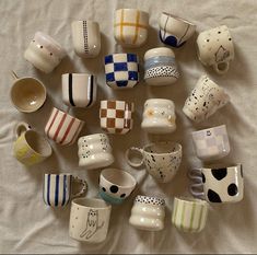 there are many coffee cups on the bed together, all different colors and designs in each cup