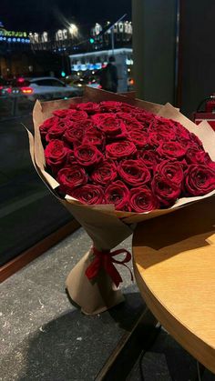 a large bouquet of red roses sitting on top of a table next to a window