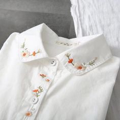 a white shirt with flowers embroidered on the chest and collar, sitting on a couch