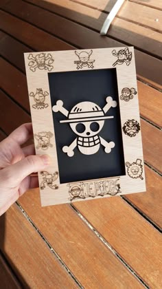 a person holding up a wooden frame with a skull and crossbones on it