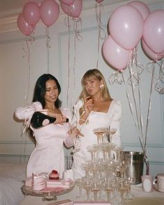 two women standing next to each other at a table with balloons and desserts on it