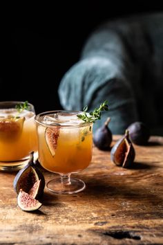 two glasses filled with drinks sitting on top of a wooden table next to figs