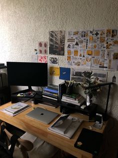 a wooden desk topped with a computer monitor and laptop next to a wall covered in pictures