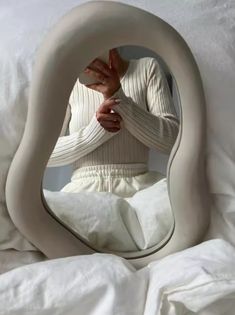 a woman sitting in bed looking at her reflection in the mirror that is shaped like a swan