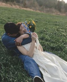 a man and woman laying on the ground hugging each other with flowers in their lap