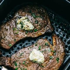 two steaks cooking in a skillet with butter and chives