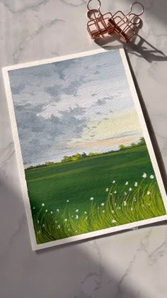 a painting of a green field with white flowers and clouds in the sky next to a pair of glasses