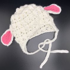 a white crocheted hat with pink ears on it sitting on a table next to a pair of scissors