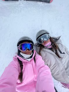 two people laying in the snow with skis on their heads and goggles on