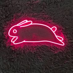 a neon sign that looks like a rabbit is on the floor in front of a black background