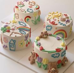 three cakes decorated with teddy bears, rainbows and numbers on white paper next to each other