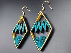 two pairs of earrings with blue and black designs on them, hanging from gold - plated hooks