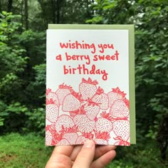 someone is holding up a birthday card with strawberries on it in front of some trees