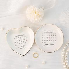 two heart shaped plates with calendars on them next to pearls and a white flower