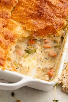 a casserole dish with meat and vegetables in it next to a piece of bread