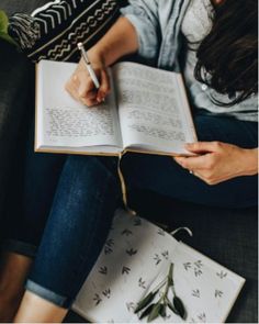 a woman sitting on a couch holding a book and writing