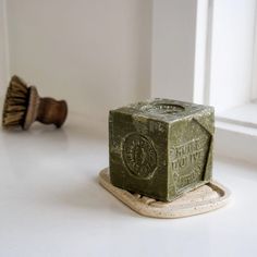 a green soap block sitting on top of a white counter next to a wooden brush