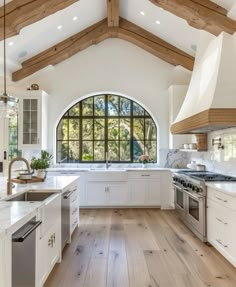 a large kitchen with an arched window and wooden beams on the ceiling, along with white cabinets