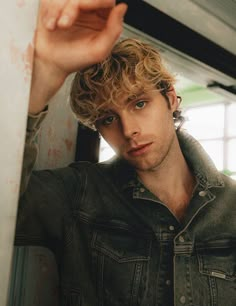 a young man with curly hair is leaning against a wall and looking at the camera