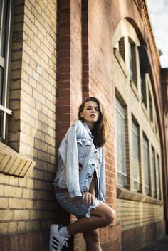 a young woman leaning against a brick wall with her legs crossed and looking off to the side