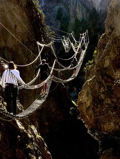 two people standing on a rope bridge over a canyon