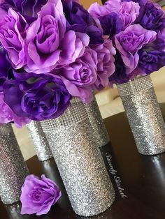 purple flowers in silver vases sitting on a table with glittered walls behind them