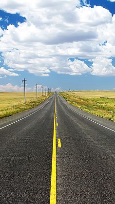 an empty road with yellow painted lines on the side and blue sky in the background