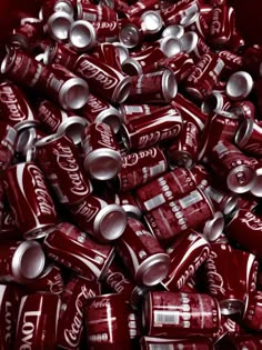 a pile of coca cola cans filled with red and silver sodas, all stacked together