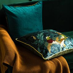 a green couch with two pillows on top of it and an orange blanket in the background