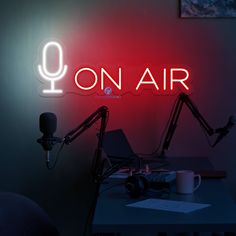 a neon sign that reads on air next to a laptop and microphone in a dark room