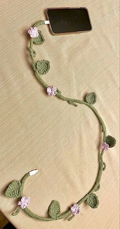 a cell phone is connected to a crocheted cord with flowers and leaves on it