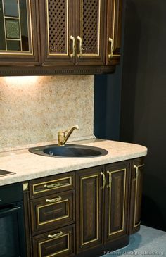 a kitchen counter with a sink and oven in it, next to cabinets that have gold trimmings on them