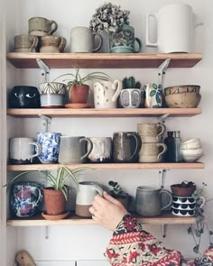 a person holding a cup in front of some shelves with coffee mugs on them