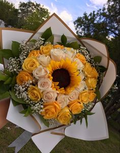 a bouquet of yellow roses and sunflowers is held by someone's hand