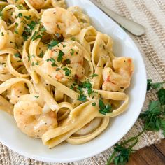 pasta with shrimp and parsley in a white bowl on a wooden table next to utensils